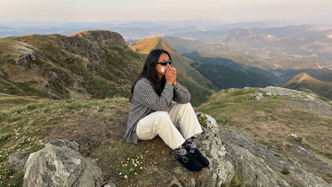 women sitting on a rock holding a daisy flower looking out on the mountains